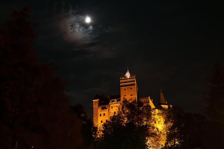 Illuminated hilltop castle glowing warmly beneath a cloudy night sky with moonlight and silhouettes.
