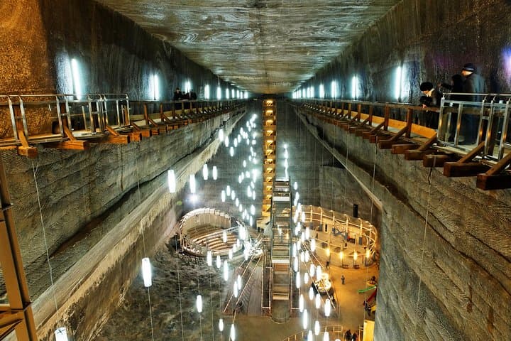 Underground salt mine chamber lit by hanging lights with wooden walkways and visitors